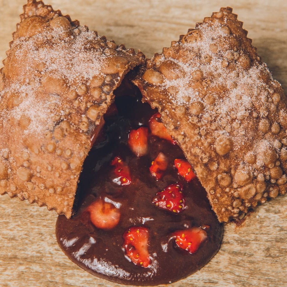 Deliciosa massa crocante recheada de brigadeiro cremoso e morangos frescos, polvilhada com açúcar e chocolate