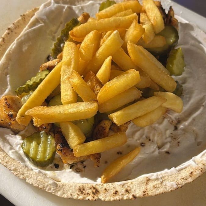 Peito de frango em cubos com pasta de alho, picles e batata frita enrolados no pão árabe.