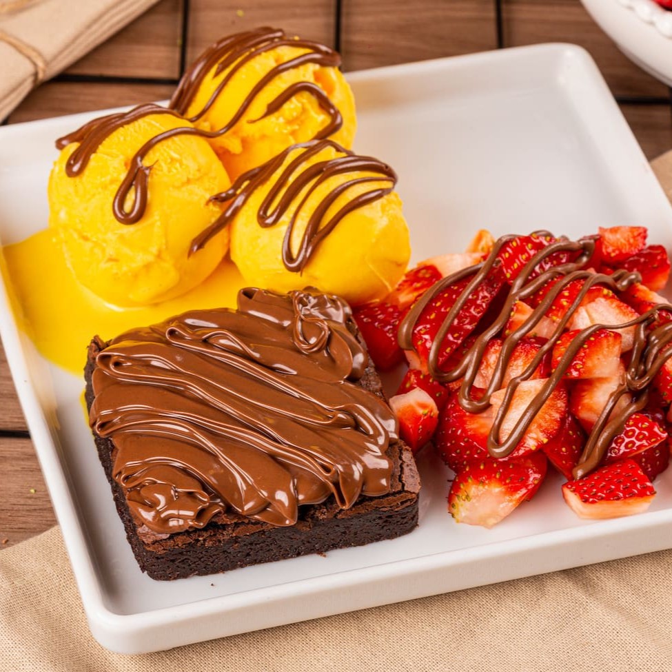 Agora, a sobremesa mais requisitada de nossa loja física pode ser montada no aconchego do seu lar, em sua versão delivery. Apresentamos o 'Brownie com Sorvete Supreme', uma combinação perfeita de um brownie tradicional, irresistivelmente saboroso, acompanhado por um pote de sorvete artesanal cremoso. O toque final fica por conta das frutas frescas e do recheio, que você tem a liberdade de escolher