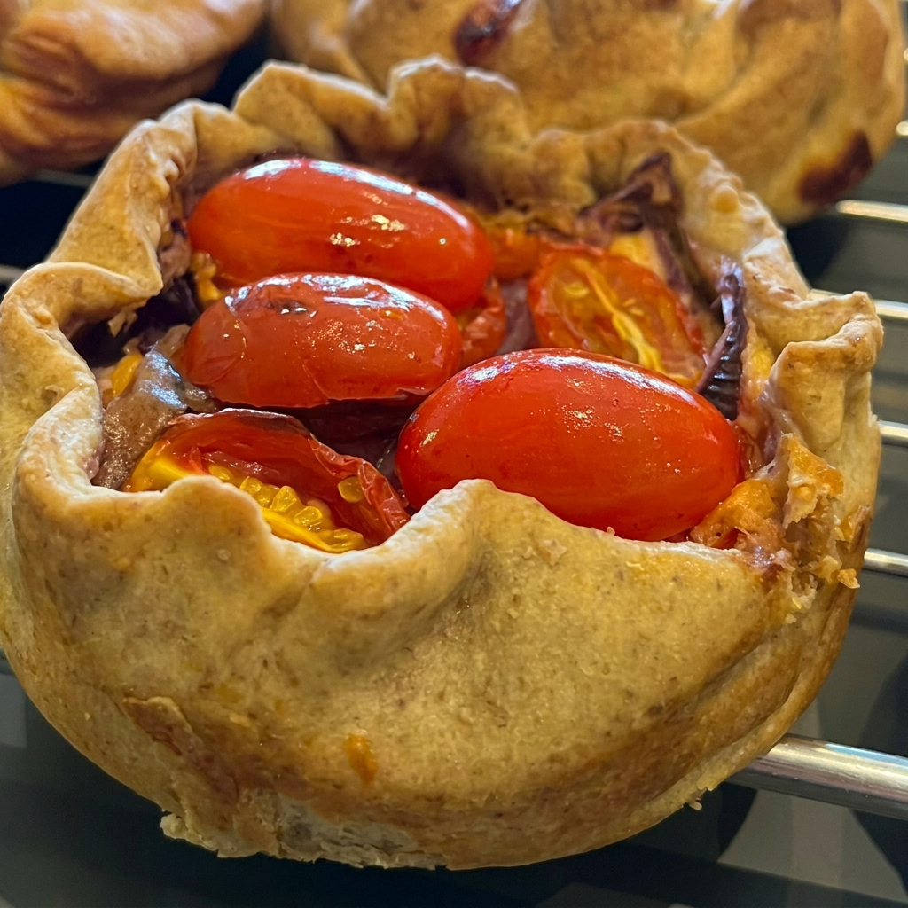 Massa patê brisée, base de queijo cremoso, parmesão com tomate cereja e cebola roxa.