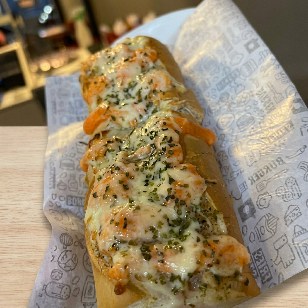 Pão francês com pasta de alho, 2 salsichas, queijo, molho e orégano.
