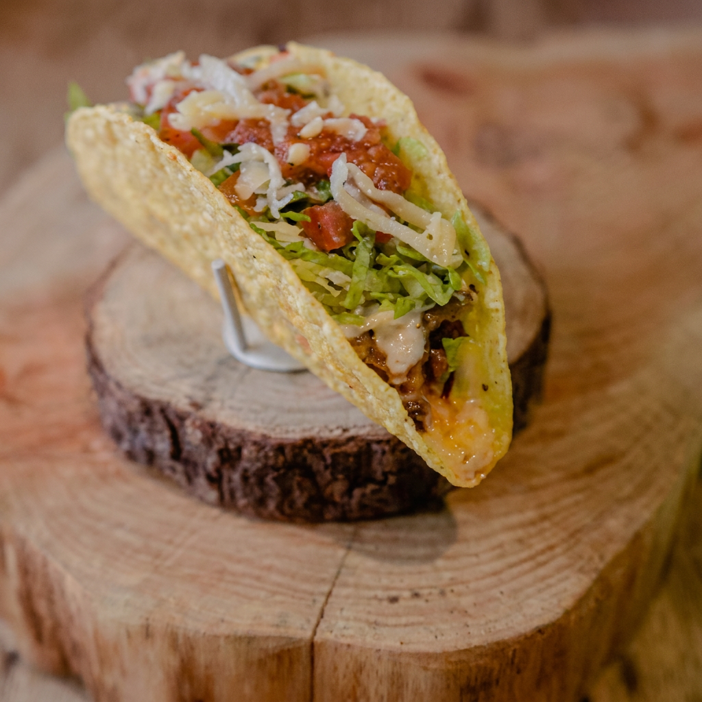 Taco de Chilli com carne -Zapata é uma homenagem à Emiliano Zapata Salazar. Este prato é uma explosão de sabor e textura, composto por um taco shell crocante, recheado com generosas porções de chilli com carne, um mix de queijos derretidos e o autêntico Pico de Gallo, trazendo a acidez e o frescor dos tomates. Para finalizar, uma camada de alface fresca que adiciona crocância e leveza. Este taco é um verdadeiro festival de sabores que irá transportá-lo diretamente para as ruas do México!