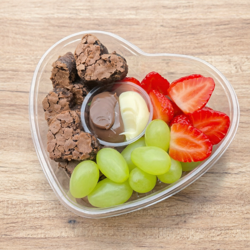 Coração gourmet composto por pedaços de brownie artesanal, morangos frescos, uvas verdes selecionadas e duo de cremes.