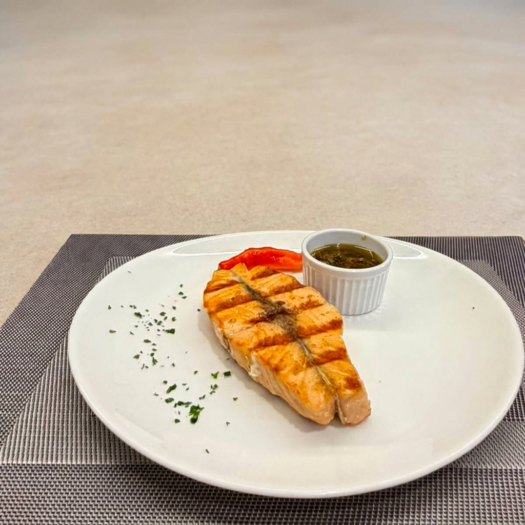 Posta de salmão chileno grelhada, finalizada com alcaparras e azeite. Opção premium para quem quer algo diferente sem sair da parrilla. 250g com dois acompanhamentos à sua escolha.