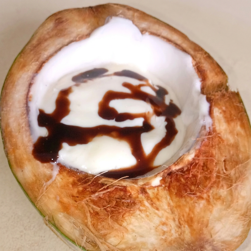 Sorvete de coco natural e coco aberto ao meio com calda de chocolate no copinho de café.