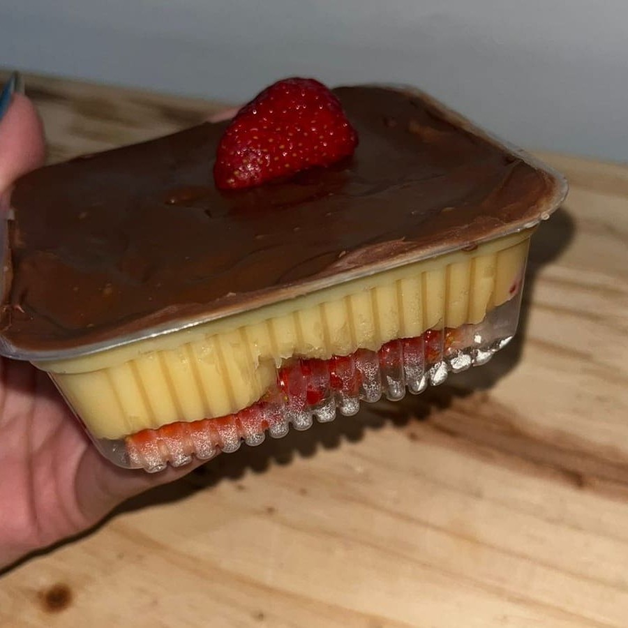 Pote com camadas de brigadeiro de Ninho com pedaços de morango e uma camada crocante de chocolate ao leite por cima.