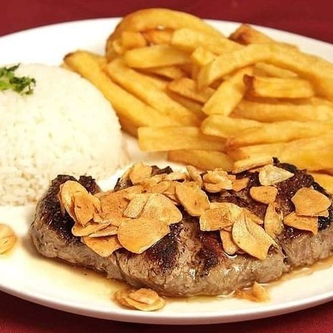 Contra filé grelhado com alhos fritos acompanha batata frita arroz branco, feijão preto e farofa.