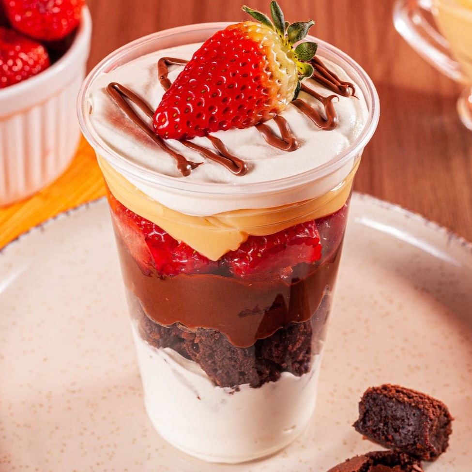 Mergulhe no paraíso com nosso irresistível Copo Mousse de Ninho com Morangos. O mousse de Leite Ninho se mistura harmoniosamente com brownie, Nutella e brigadeiro cremoso de Leite Ninho, abraçando morangos frescos. Essa explosão de sabores, finalizada com fios de Nutella e morangos, é uma experiência que você não pode perder.