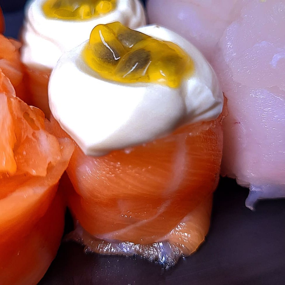 Enrolado de salmão com arroz, finalizado com cream cheese e polpa de maracujá.