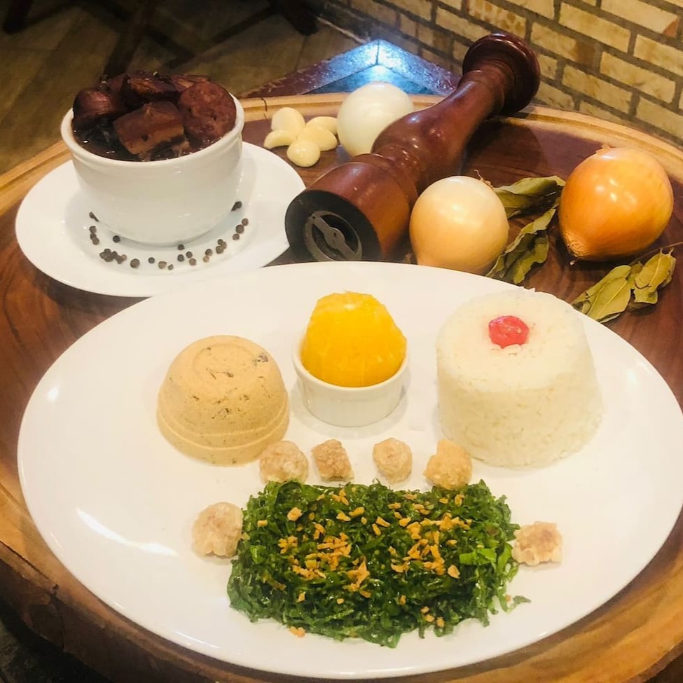 A 'Feijoada Executiva - 308' é uma autêntica mini refeição que honra a tradição brasileira. Composta por feijão preto enriquecido com uma variedade de carnes salgadas e suculentas, esta feijoada é realçada pelo sabor robusto da linguiça e a crocância do torresmo. Acompanha um arroz branco soltinho, couve refogada ao alho que traz frescor ao prato e a laranja, acrescentando um toque de acidez. Este prato é uma homenagem à riqueza da culinária nacional, preparado com cuidado e carinho para a sua satisfação.