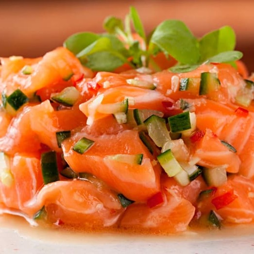 "Salmão em cubos, temperos orientais, cebolinha e gergelim.  ""Tartar de salmão fresco em cubos delicados, cuidadosamente temperados com especiarias orientais que realçam o sabor natural do peixe. Finalizado com cebolinha fresca e uma pitada crocante de gergelim, esse prato oferece uma combinação perfeita de texturas e aromas que conquistam o paladar a cada garfada."""