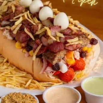 "Cachorro Quente - 2 Salsinhas, molho '' cebola e tomate "" bacon, calabresa, presunto, muçarela, ervilha, milho, uva passas, azeitona, ovo de codorna, batata palha, queijo ralado, ketchup, maionese, mostarda e maionese temperada da casa."