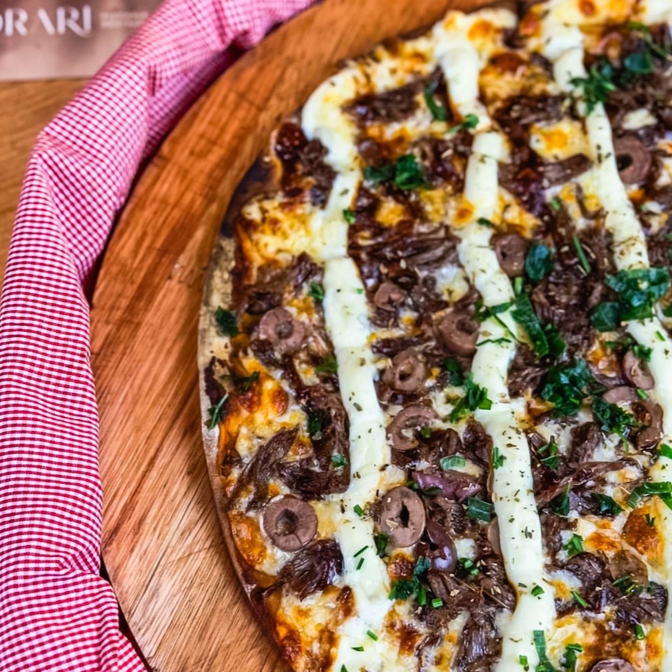 Desfrute da nossa 'La Bella (Costela) - Pizza da Casa - 40 cm', uma das estrelas da categoria 'As Queridinhas'. Essa delícia é preparada com uma massa artesanal macia e crocante, coberta pelo exclusivo molho da casa. Acrescentamos uma generosa camada de mussarela derretida, que se funde perfeitamente com a suculenta costela bovina. O toque especial fica por conta das azeitonas pretas, que proporcionam um sabor singular. Regamos com um delicioso molho barbecue para intensificar ainda mais o sabor. A cremosidade do legítimo Catupiry e a frescura do cheiro verde contrastam maravilhosamente, enquanto o orégano dá o toque final a este espetáculo de sabor. Uma verdadeira tentação para os paladares mais exigentes!