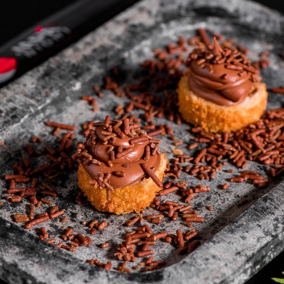 Deliciosa rodela de banana empanada, sobreposto por chocolate e granulado.