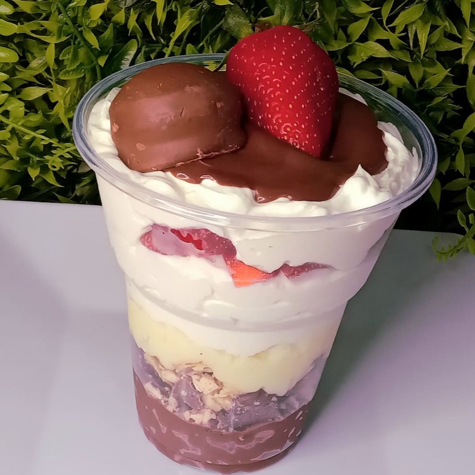 O copo da felicidade vem com camada de brigadeiro, bombom Sonho de Valsa, brigadeiro branco, morangos picados e mousse de leite Ninho, finalizado com ganache de chocolate bombom Sonho de Valsa e morango