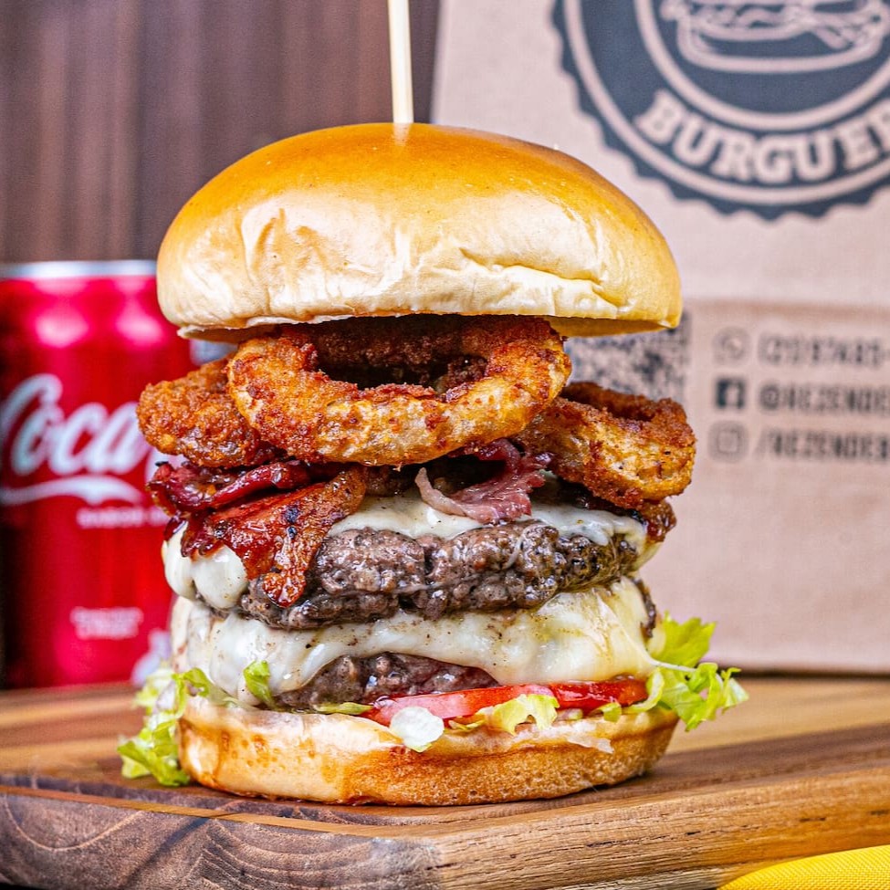 Pão brioche, 2 carnes artesanais de 150g, 2 fatias de queijo mussarela, bacon fatiado, salada, 3 anéis de cebola e maionese especial