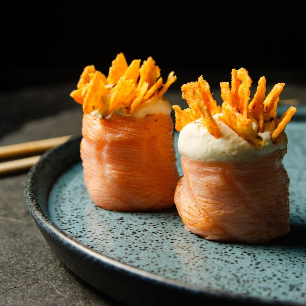 Salmão maçaricado enrolando arroz com cream cheese e um toque de Doritos.