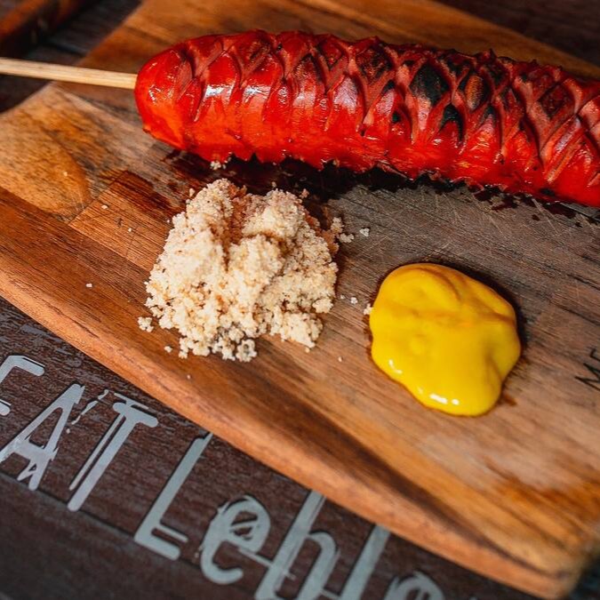 1 unidade de espeto de salsichão acompanhada de farofa de bacon e molho barbecue.