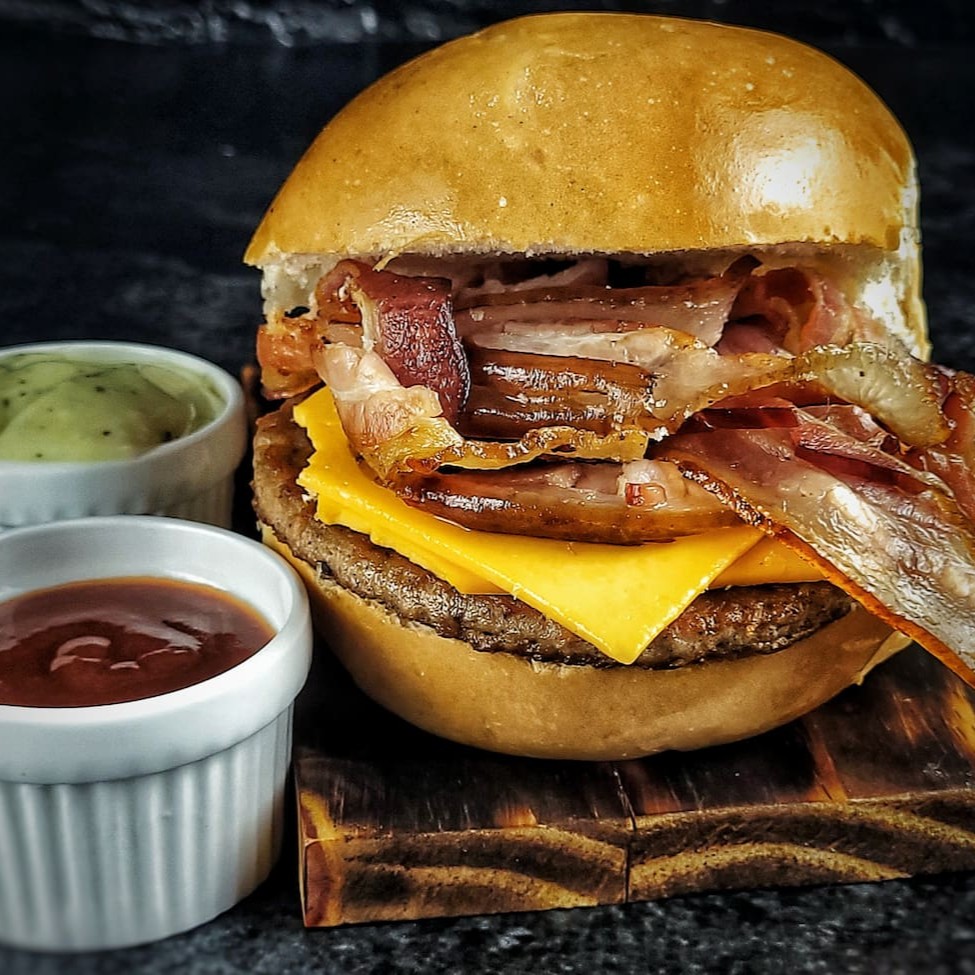 O Russo Bacon é uma inigualável seleção da nossa categoria ' Sanduíches Americanos'. Apresentando um pão bola fresquinho e aconchegante, abriga uma carne macia e suculenta. O queijo cheddar derretido de  primeira qualidade, proporciona uma união sublime de sabores. A dupla camada de bacon crocante é complementada pelo adocicado do ketchup e nosso molho especial da casa, que traz um toque secreto e irresistível