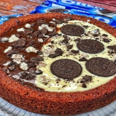 Apresentamos a você o nosso divino Bolo Piscina de Oreo. Um bolo generoso, pesando 1,2kg, cuidadosamente concebido para proporcionar 16 fatias de pura indulgência. Esta delícia é metade coberta com uma suave e cremosa cobertura de Ninho, enquanto a outra metade é adocicada pela riqueza do nosso incomparável brigadeiro caseiro. Para finalizar, a obra-prima é polvilhada com Oreo picotado, proporcion