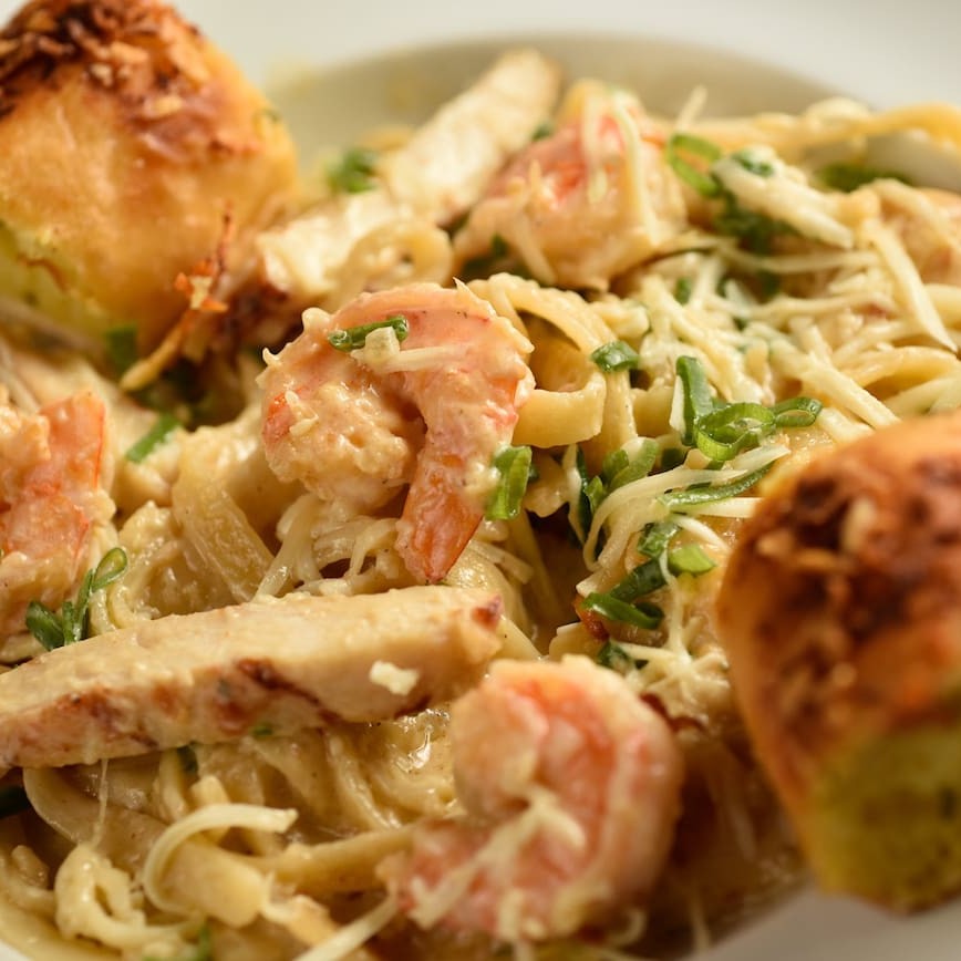Saboroso talharim com camarão e tiras de frango junto ao molho alfredo. Acompanha pão de alho.