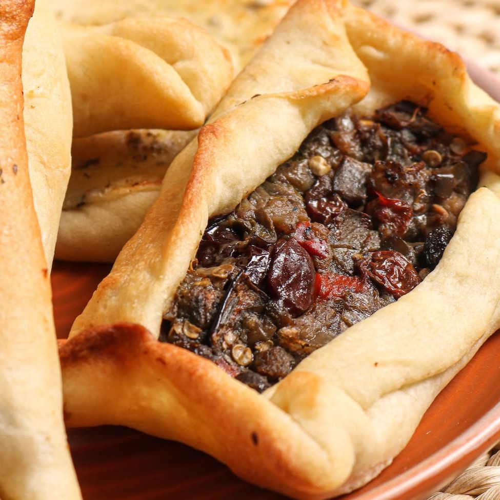 Esfiha de Caponata com Berinjela - Vegana: uma massa leve e dourada, recheada com um saboroso mix de berinjela, pimentões vermelhos, cebola e azeitonas, temperados com ervas aromáticas e um toque de azeite. Uma combinação rica em sabores e 100% vegana, que agrada tanto veganos quanto amantes da boa comida!