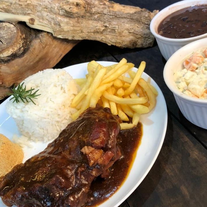 Saborosa costela suína temperada no exclusivo dry rub da casa e defumada por 6 horas, garantindo suculência e sabor único. Acompanha arroz soltinho, feijão fresquinho, farofa crocante, maionese e sua escolha entre batata frita ou aipim frito. Uma experiência gastronômica completa!