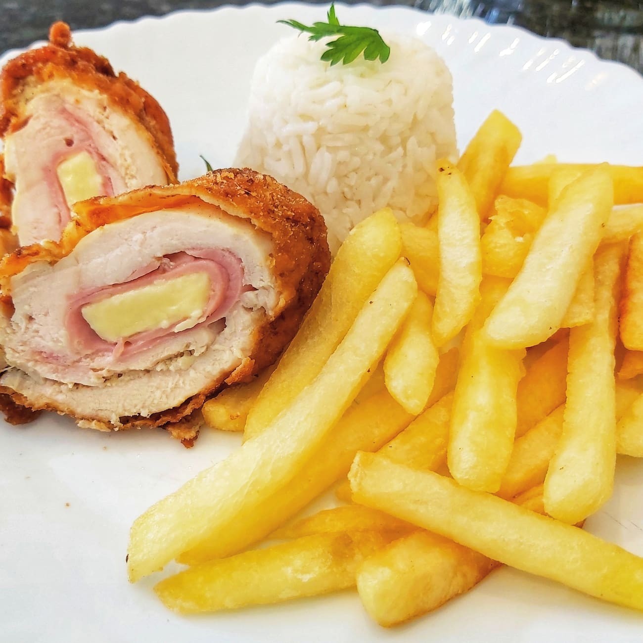 Filé de frango a milanesa recheado com queijo e presunto.  Acompanhamentos: arroz, feijão, macarrão, farofa, fritas e salada.
