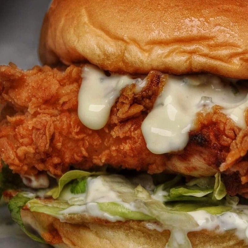 Pão brioche selado, frango empanado e frito, cheddar da casa, alface, tomate, cebola roxa e barbecue.