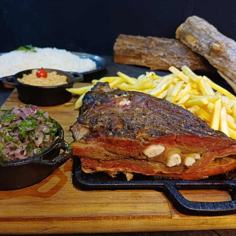 Uma suculenta costela bovina de cerca de 550g, minuciosamente temperada com nosso dry rub exclusivo e defumada por longas 8 horas em lenha frutífera. Acompanha farofa de bacon crocante, 500g de arroz e a sua escolha entre 500g de batata ou aipim frito. Escolha seus acompanhamentos abaixo