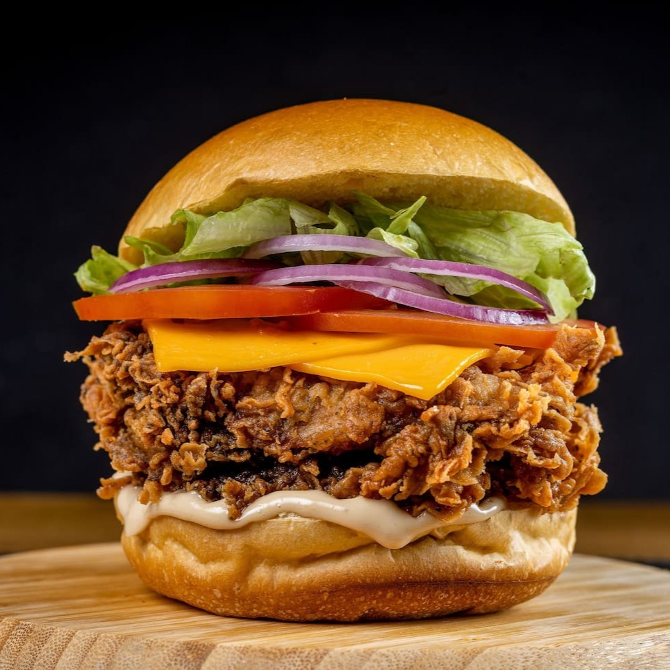 Filé de sobrecoxa crispy (ou 2 filezinhos de peito) com queijo cheddar, molho grill, alface americana crocante, tomate fresquinho e cebola roxa — tudo no pão de brioche macio. Crocância e frescor na mordida que vai te conquistar!