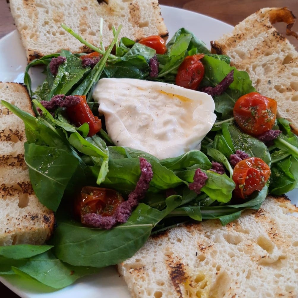 Burrata, Acompanha salada de rúcula, tomatinhos, molho pesto e tapenade, com Focaccia de fermentação natural  Contém Glúten Contém Lactose