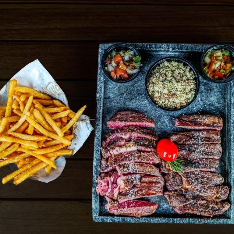 Porção de 440g fatiada de bife ancho na brasa. Acompanha farofinha de alho, batata frita e molho à campanha.