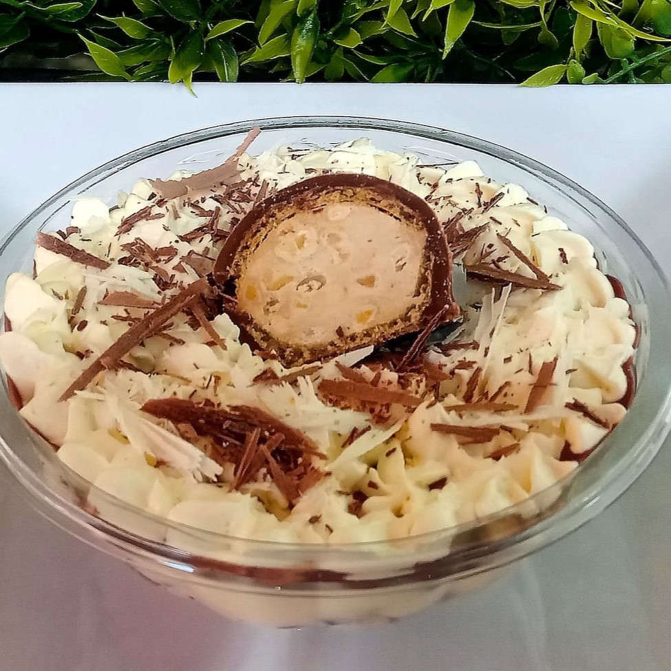 Creme branco cremoso, camada de bombom Sonho de Valsa picado, ganache de chocolate, coberto com chantilly trufado e finalizado com raspas de chocolate e bombom