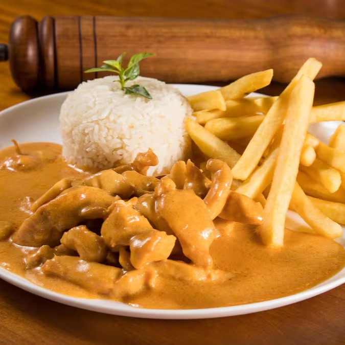 Cubos macios de frango no molho mais cremoso da sua vida, com champignon, segredos da casa e nosso sugo artesanal. Servido com arroz branco soltinho e batata super crocante. Conforto e sabor em cada garfada.