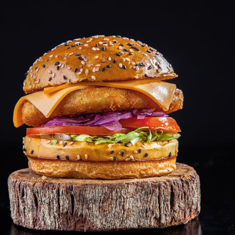 Pão Brioche Gergelim, hamburguer de frango empanado, fatia queijo cheddar, salada e maionese surreal