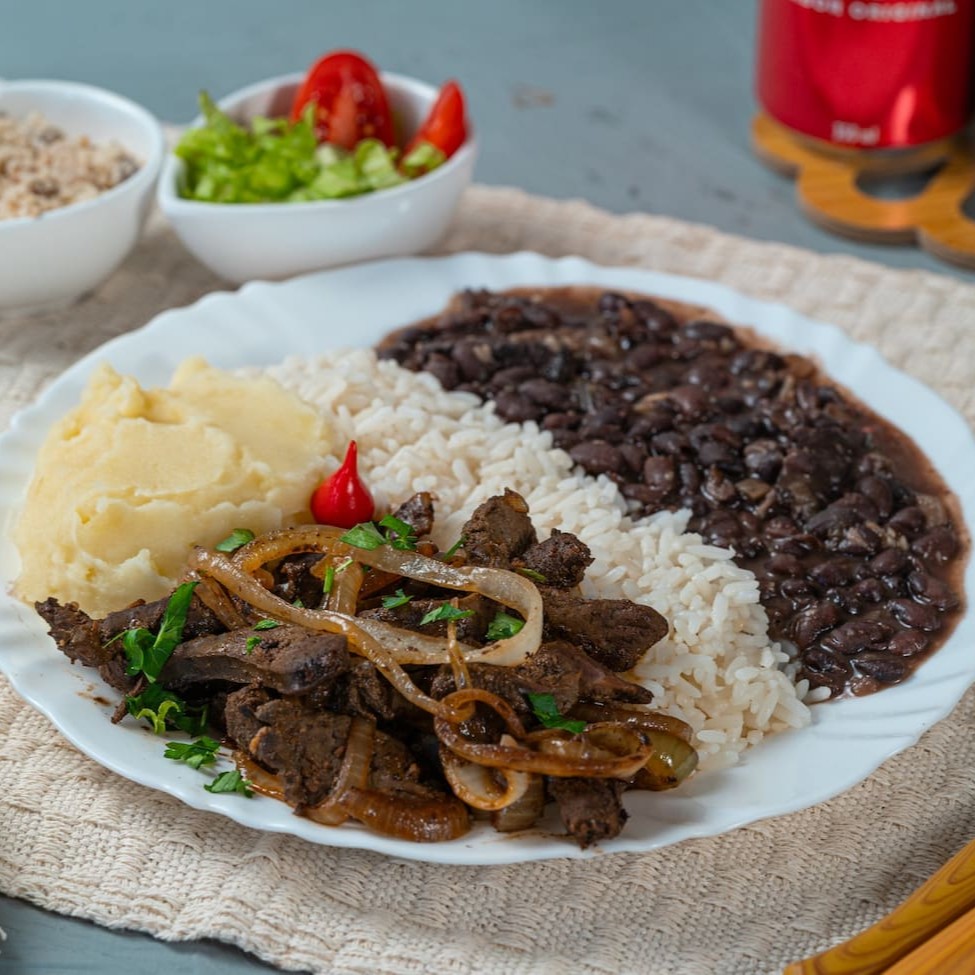 Fígado macio e bem temperado, grelhado no ponto certo e coberto com cebolas douradas e suculentas. Acompanha purê de batata cremoso, arroz soltinho, feijão caseiro saboroso, farofa crocante e uma salada fresquinha para equilibrar os sabores. Uma refeição nutritiva e cheia de sabor!