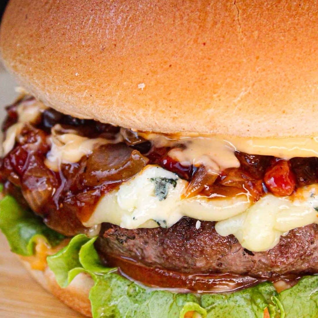 Pão de Brioche, 130g de Blend da Maju, gorgonzola, muçarela, bastante bacon, cebola caramelizada, alface, tomate e molho.