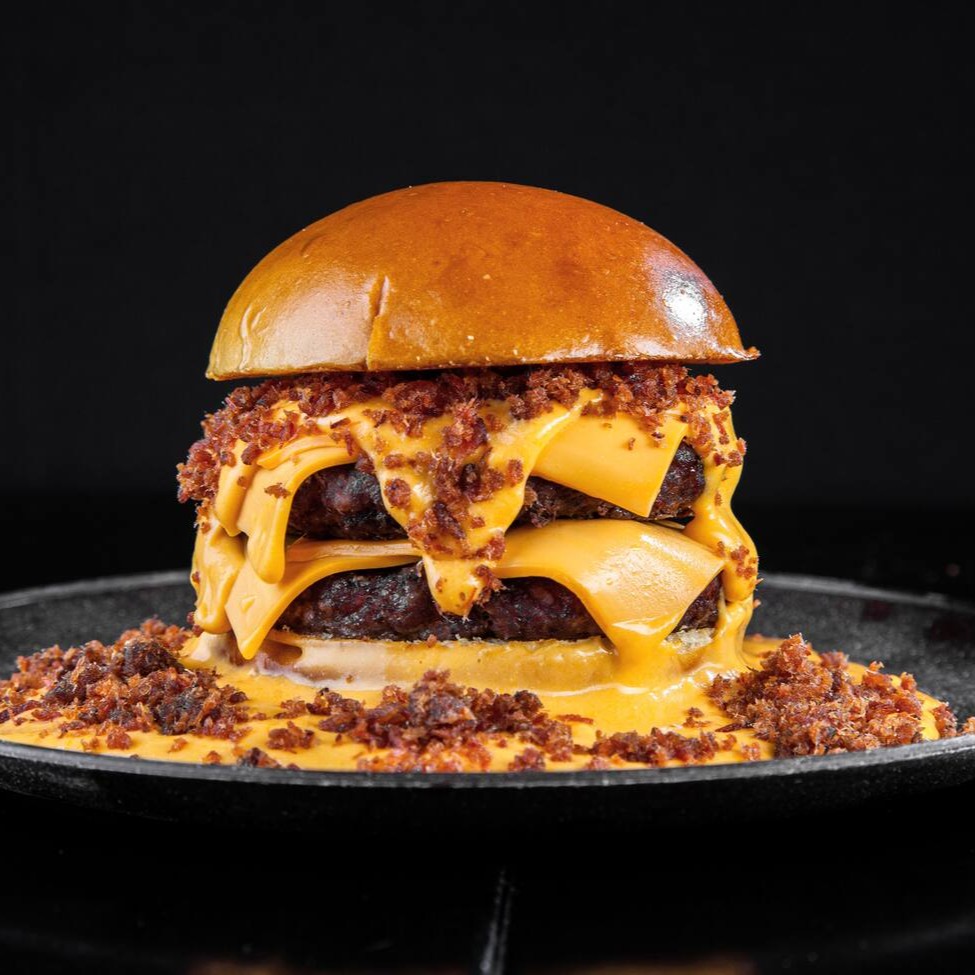 Carro chefe da casa!  Pão brioche Gold, 2 blends bovinos 120g, fatias de queijo cheddar, coberto com creme cheddar espetacular e finalizado com farofa de bacon.