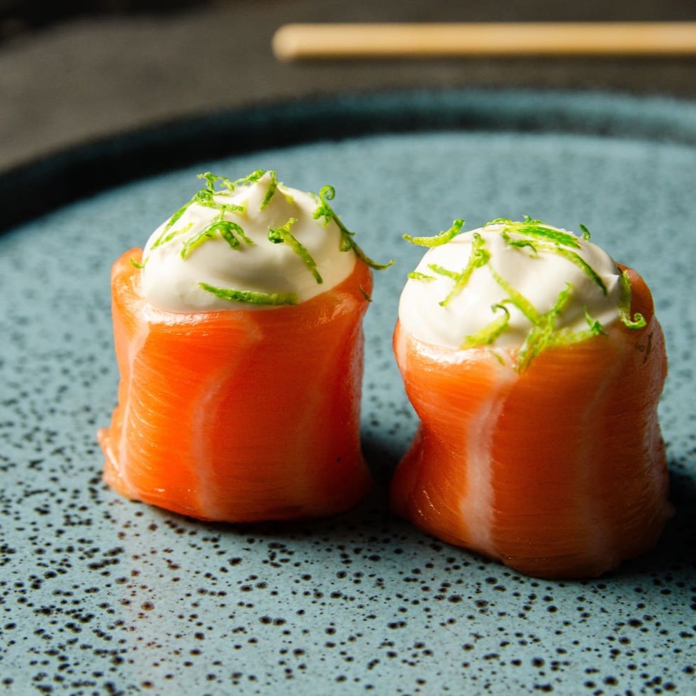 Salmão enrolando arroz com cream cheese e um toque com raspas de limão.