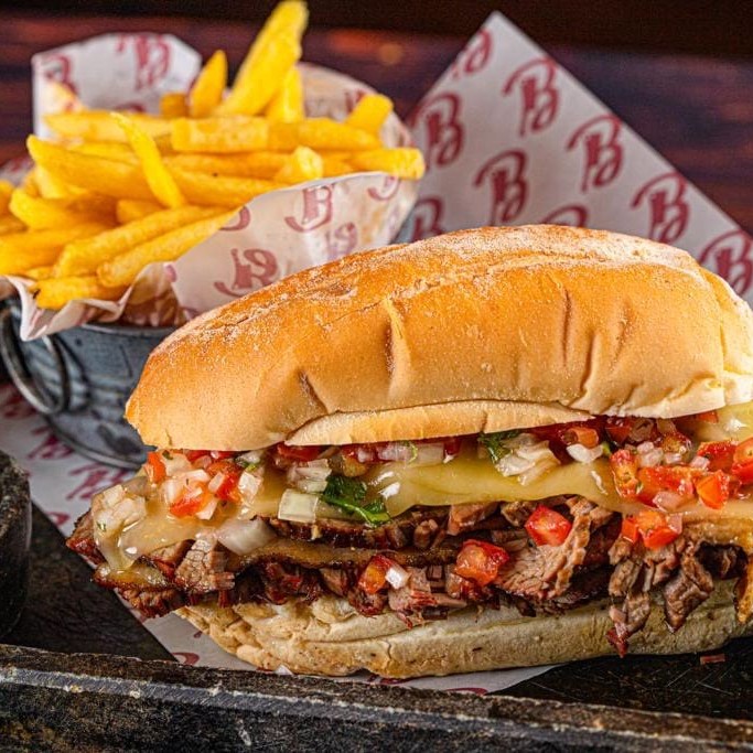 Peito bovino Black angus defumado no pit por 12h com lenha pecan, molho de queijo muçarela e vinagrete. Servido na baguete francesa