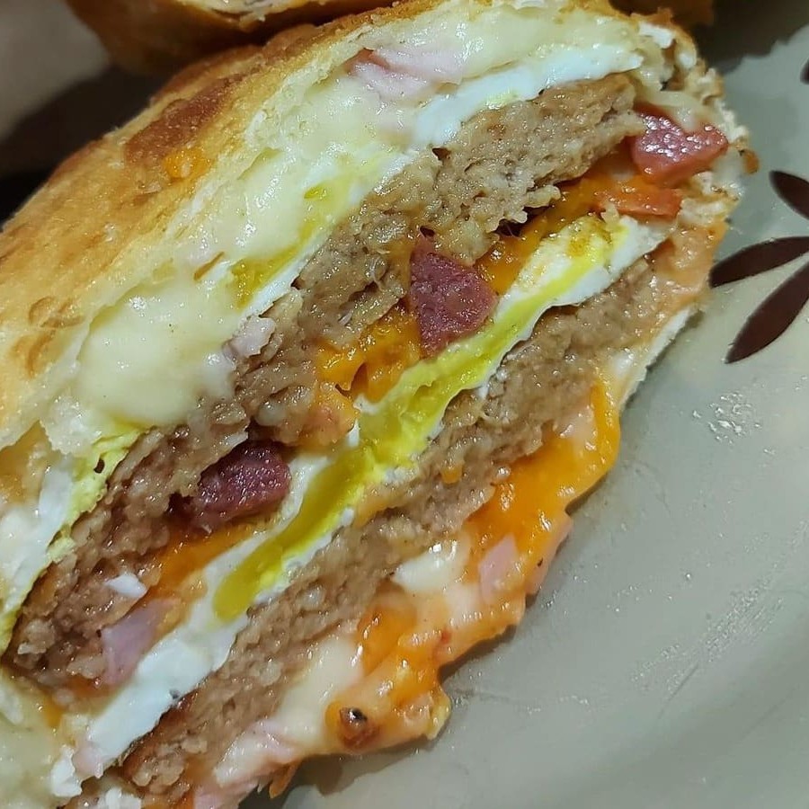 Feito com duas generosas camadas de carne de hambúrguer, o prato é enriquecido com ovo macio, queijo derretido, fatias de presunto suculentas e crocantes pedaços de bacon. A calabresa adiciona um toque picante irresistível, enquanto o cheddar e o Catupiry, cremosos e saborosos, finalizam essa obra-prima gastronômica.