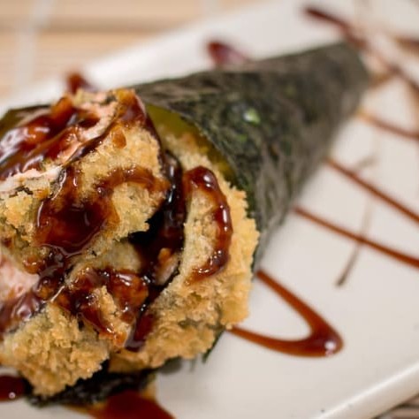 """Temaki Super Hot Double Cheese Maçaricado preparado com alga crocante, arroz temperado no ponto certo e generosa porção de salmão envolto em molho levemente apimentado. Recheado e coberto com dupla camada de cream cheese, finalizado no maçarico para trazer cremosidade extra e aquele sabor defumado irresistível. Enrolado na hora para garantir frescor, crocância e uma explosão de sabores a cada mordida — perfeito para quem ama intensidade e cremosidade na culinária japonesa."""