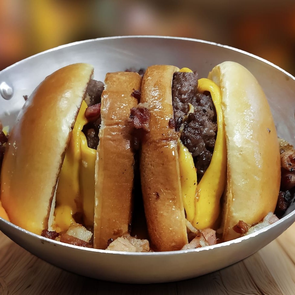 Pão brioche, blend bovino de 150g Artesanal e queijo cheedar, partido ao meio mergulhado em cheedar cremoso com bacon em cubos.