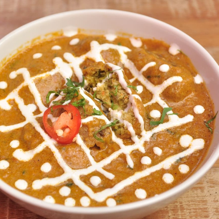 Uma especialidade do norte da índia. bolinhos de vegetais e ervilhas cozidos em um suave molho de tomate, cebola, castanha de caju e creme de leite.