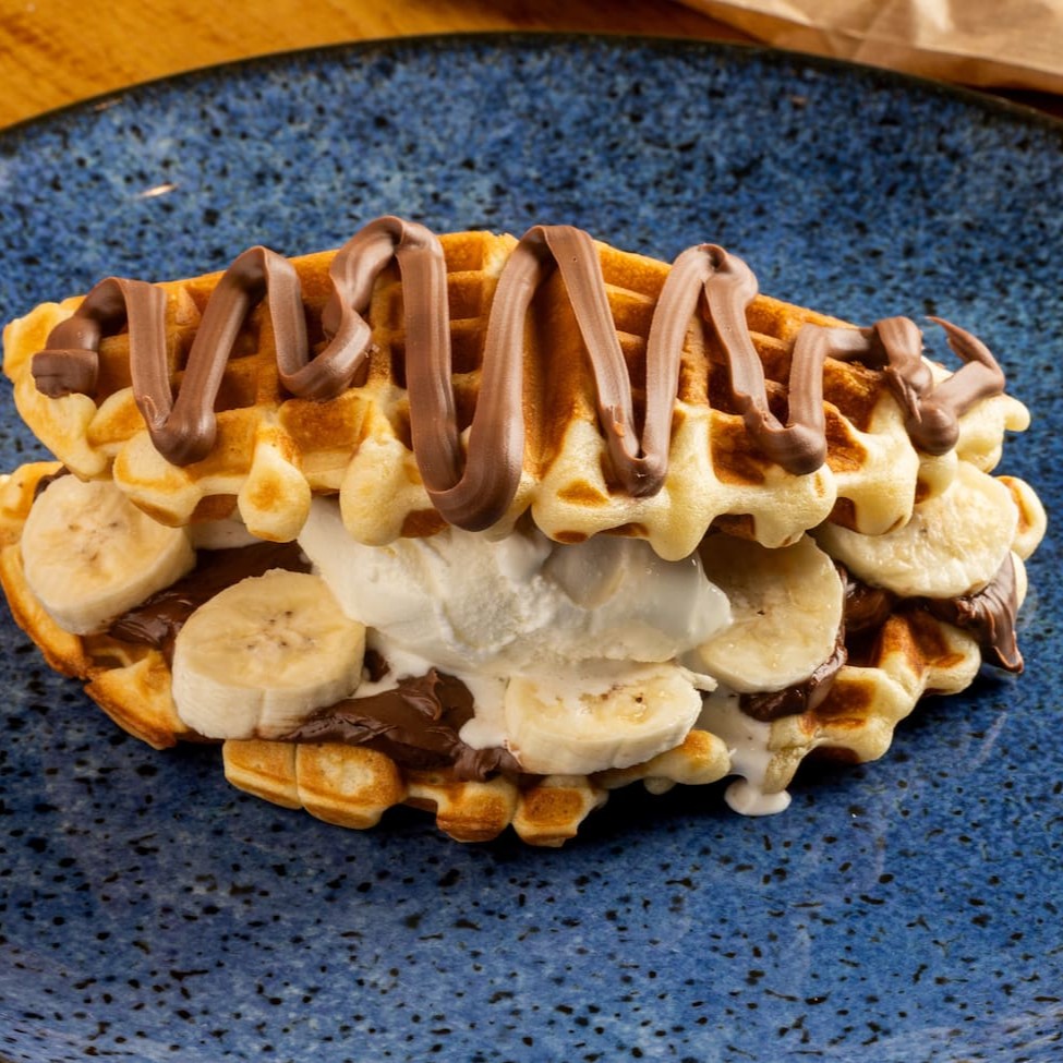 Nosso delicioso waffle em formato de sanduíche recheado com Nutella, banana e sorvete. O sorvete é enviado em uma embalagem a parte.