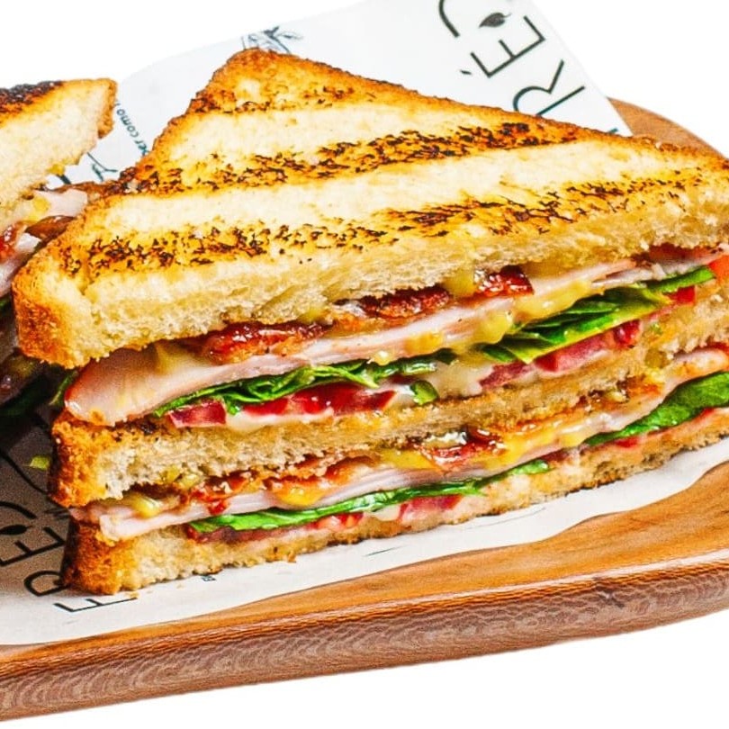 "Inspirado no famoso ""Clube Sanduíche"". Três fatias generosas de nosso Pão Suíço tostadas, Peito de Peru, Tomate, Rúcula e Maionese de Curry leve com Bacon Crocante  *Nossas produções são todas feitas na casa *Pães de Fermentação Natural"