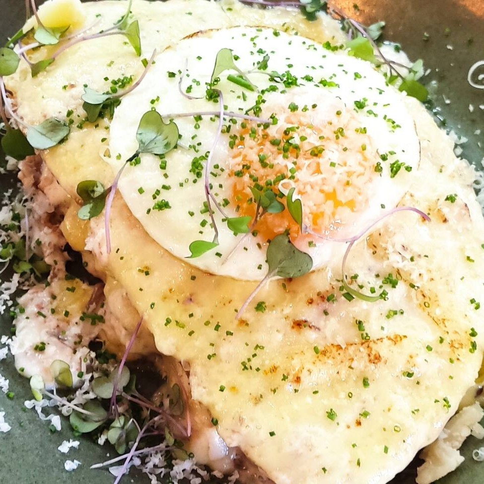 Fatia de pão Sourdough/ Carne desfiada/ Queijo emmental/ Bechamel de bacon/ Ovo frito (gema mole) Obs: O ovo frito poderá ter gema estourada ou passar do ponto (devido ao calor na embalagem), durante o transporte.