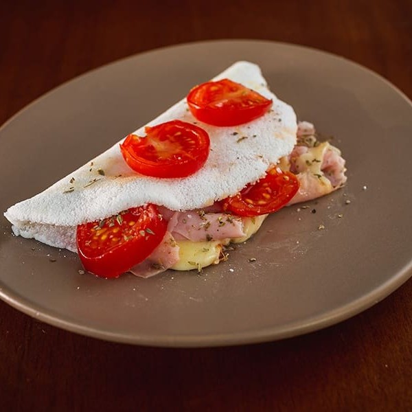 Recheada com presunto saboroso, queijo à sua escolha (minas, coalho, mussarela, requeijão ou cheddar), tomate cereja fresquinho e um toque especial de orégano que perfuma e realça o sabor. Perfeita para quem ama pizza, mas não abre mão da leveza e do sabor único da nossa massa de tapioca.