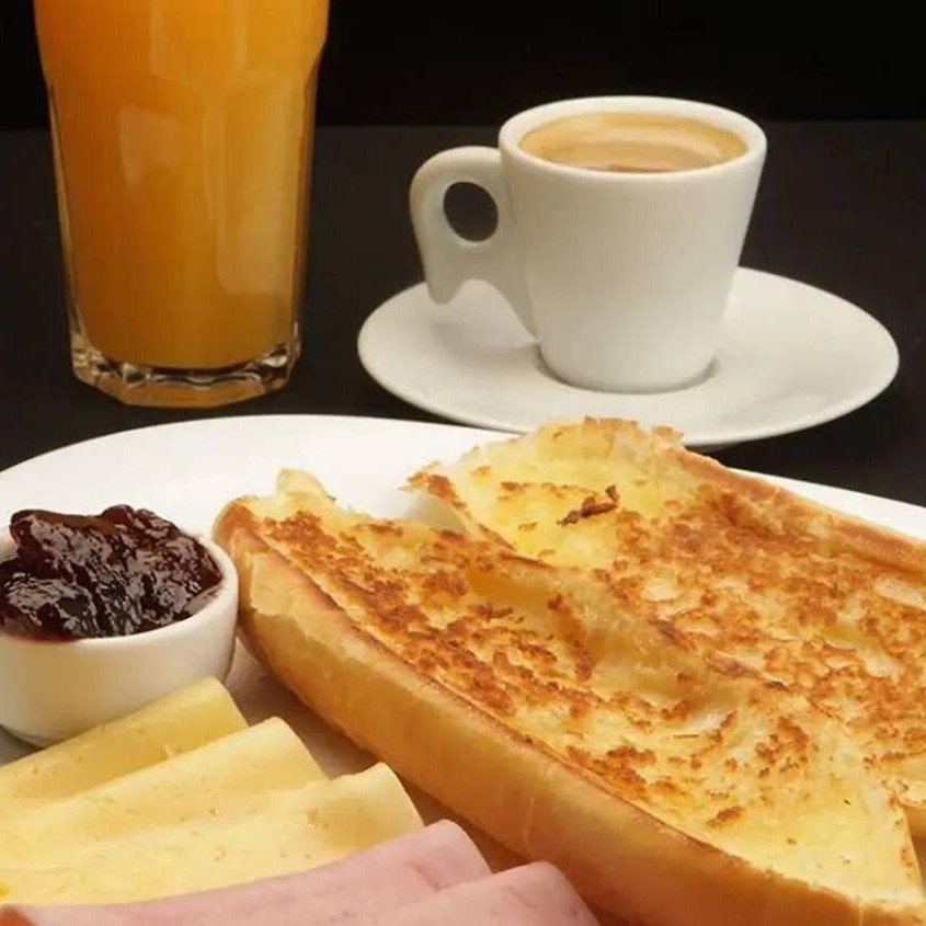 Você pode escolher entre um intenso café expresso, um suave café coado ou um refrescante suco de laranja de 300ml, todos preparados com carinho para atender seu gosto.  Acompanhando a bebida, servimos uma baguete quentinha, tostada na chapa, com sua escolha de manteiga cremosa ou doce geleia de morango, oferecendo uma combinação perfeita de texturas e sabores. Para complementar, incluímos uma fatia de presunto e uma fatia de queijo minas fresquinho, garantindo o equilíbrio ideal entre proteínas e carboidratos *Foto ilustrativa
